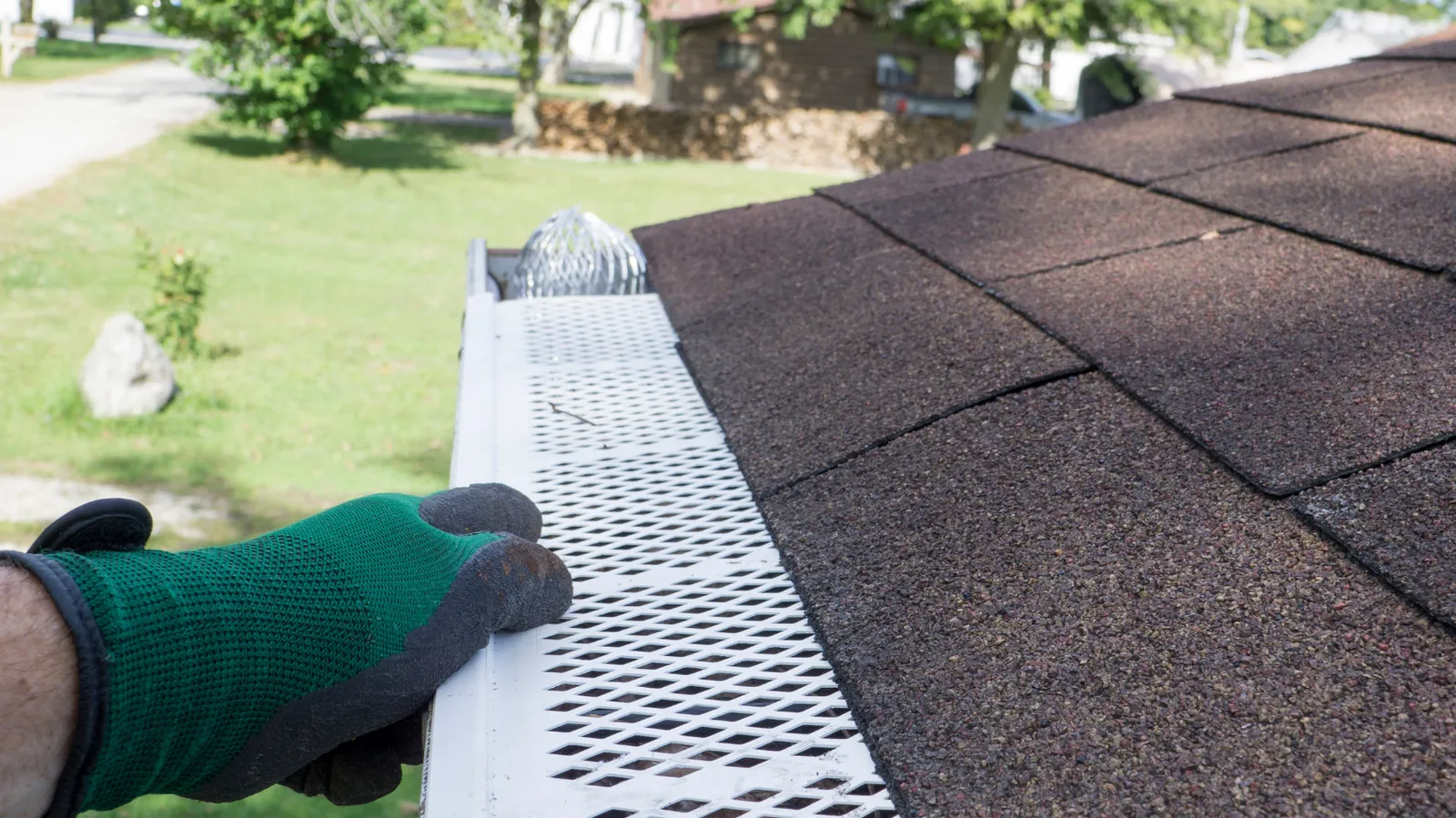 Perforated gutter guard secured by a roofer's gloved hand